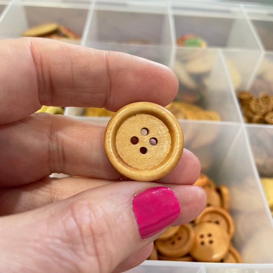 Hand holding a gold button with a blurred background of button collection