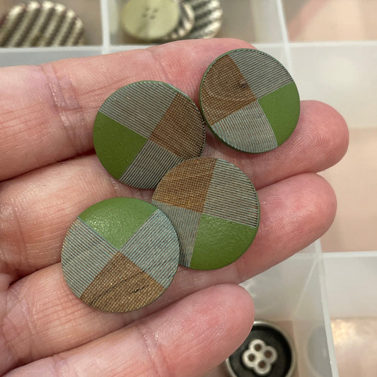 Hand holding three green and brown patterned buttons with a container of buttons in the background.
