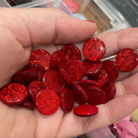 Hand holding red glittery buttons with a container of various buttons in the background