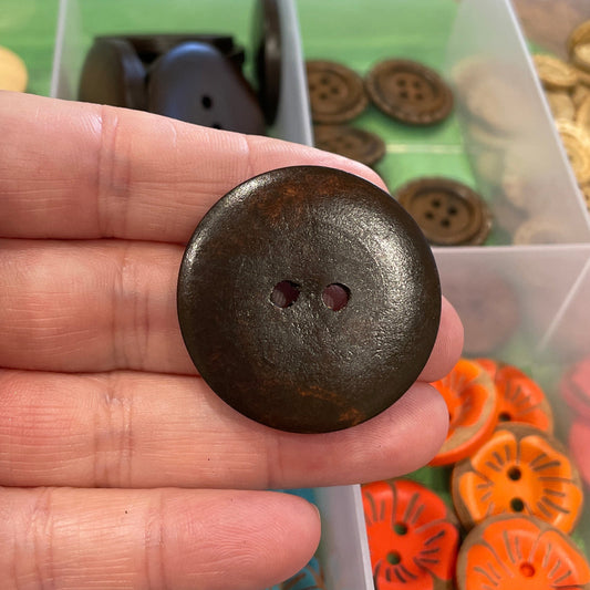 Hand holding a brown button with a container of colorful buttons in the background