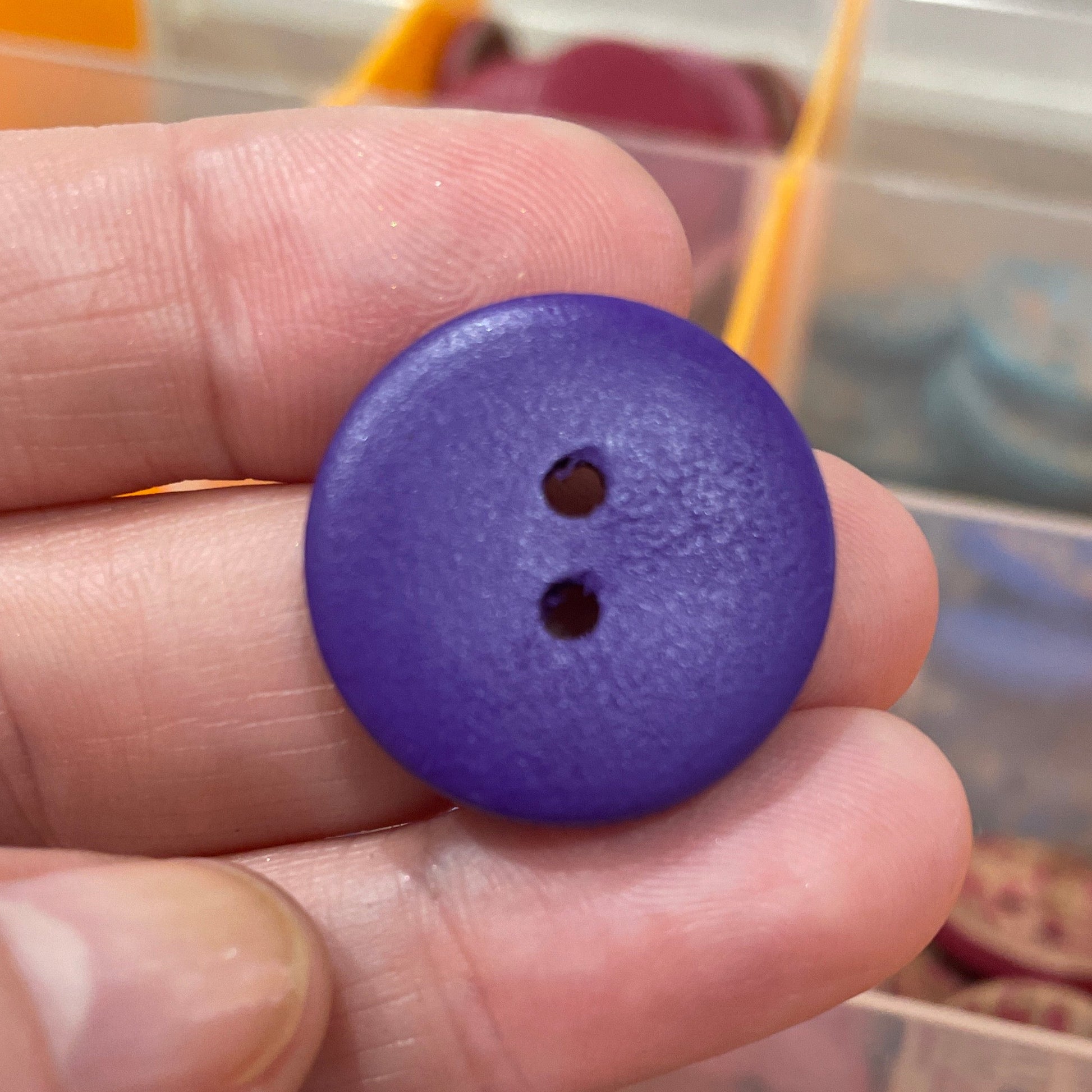 Purple button held between fingers with a container of buttons in the background