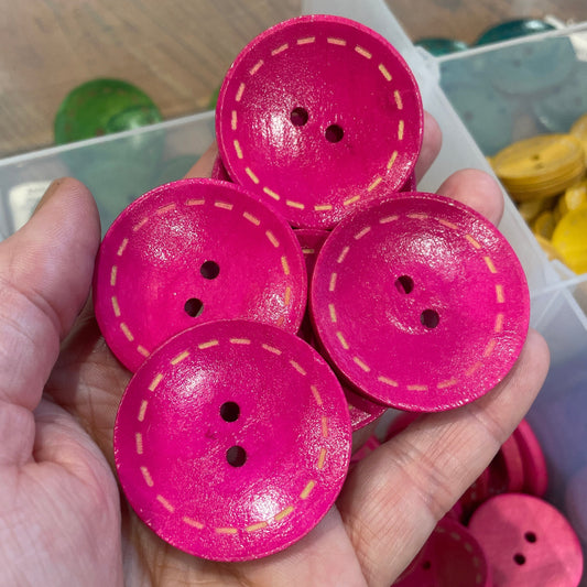 Hand holding pink buttons with a clear container in the background