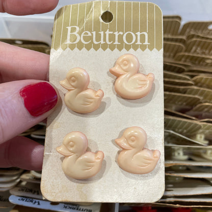 Set of small duck-shaped buttons on a Beutron branded card held by a hand with red nail polish.
