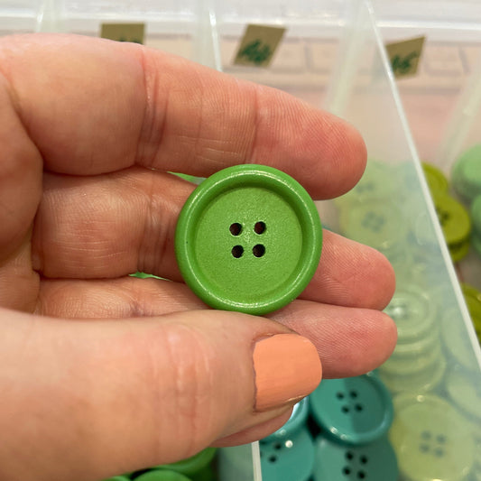 Hand holding a green button with a container of green buttons in the background