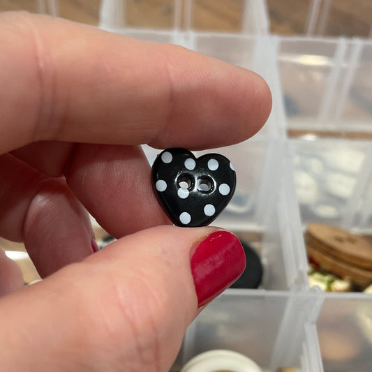 Hand holding a black and white button with a container of buttons in the background