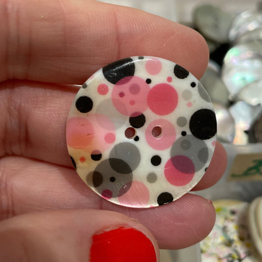 Polka dot button held by a hand with red nail polish, against a blurred background of buttons.