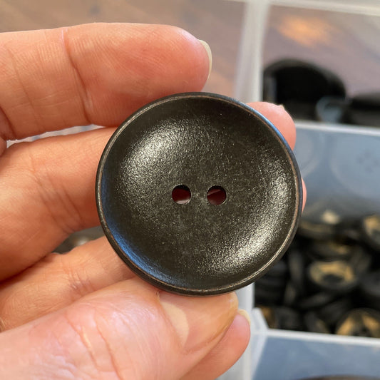 Hand holding a dark brown button with a blurred background of buttons.