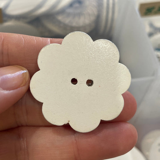 Hand holding a white flower-shaped button with a blurred background of more buttons.