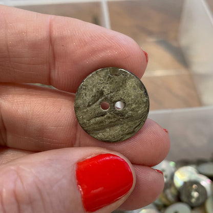 Hand holding a small button with a container of buttons in the background