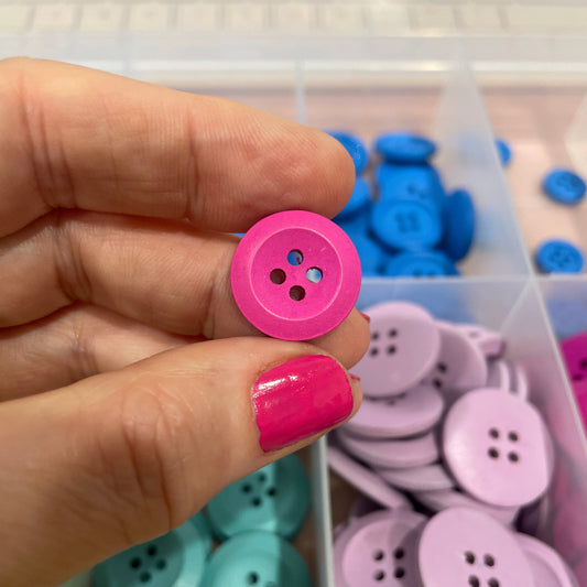 Hand holding a pink button with a container of colorful buttons in the background