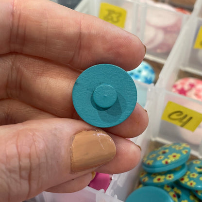 Hand holding a blue button with a container of colorful buttons in the background