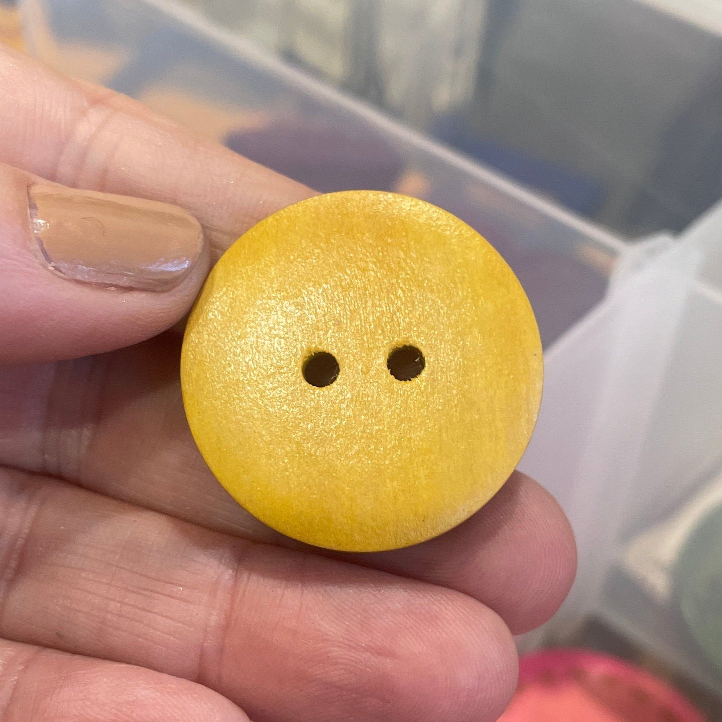 Yellow button held by a hand with a container of colorful buttons in the background