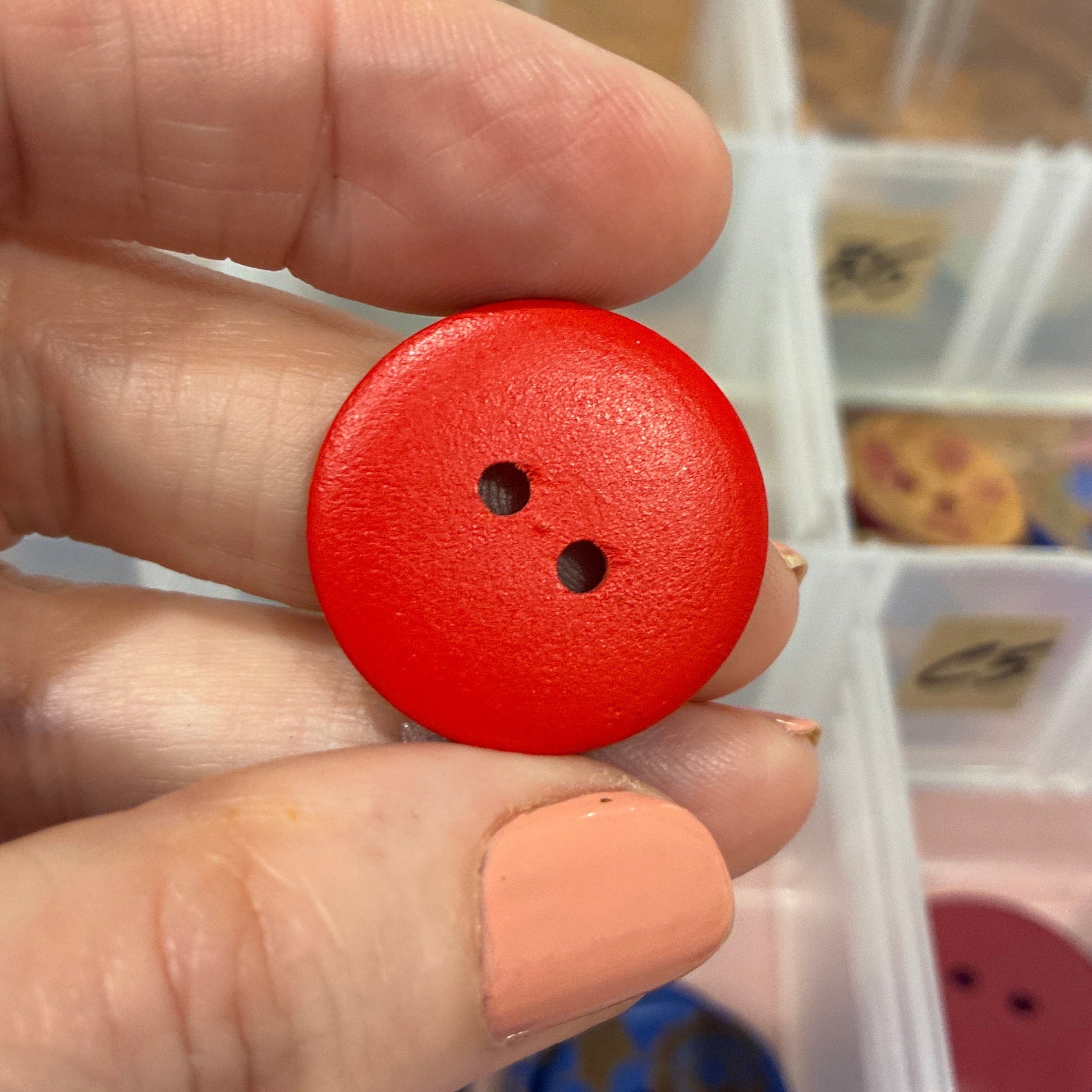 Red button held between fingers with a container of buttons in the background