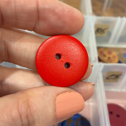 Red button held between fingers with a container of buttons in the background