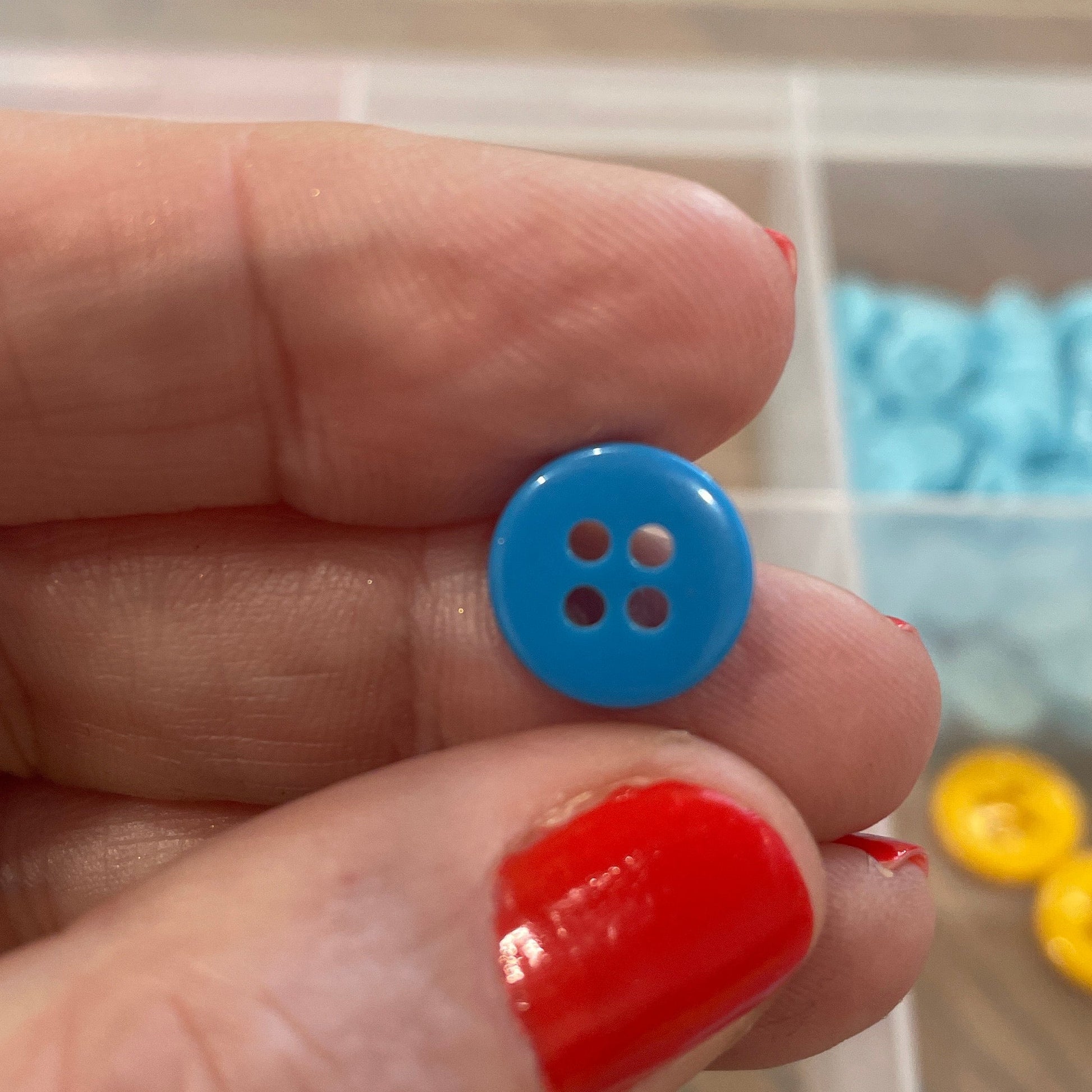 Hand holding a blue button with a container of colorful buttons in the background