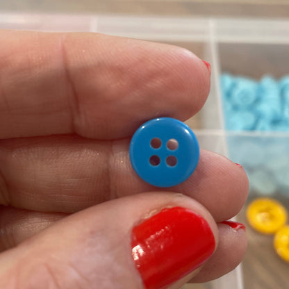 Hand holding a blue button with a container of colorful buttons in the background
