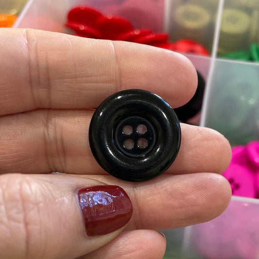 Black button held by a hand with a colorful assortment of buttons in the background