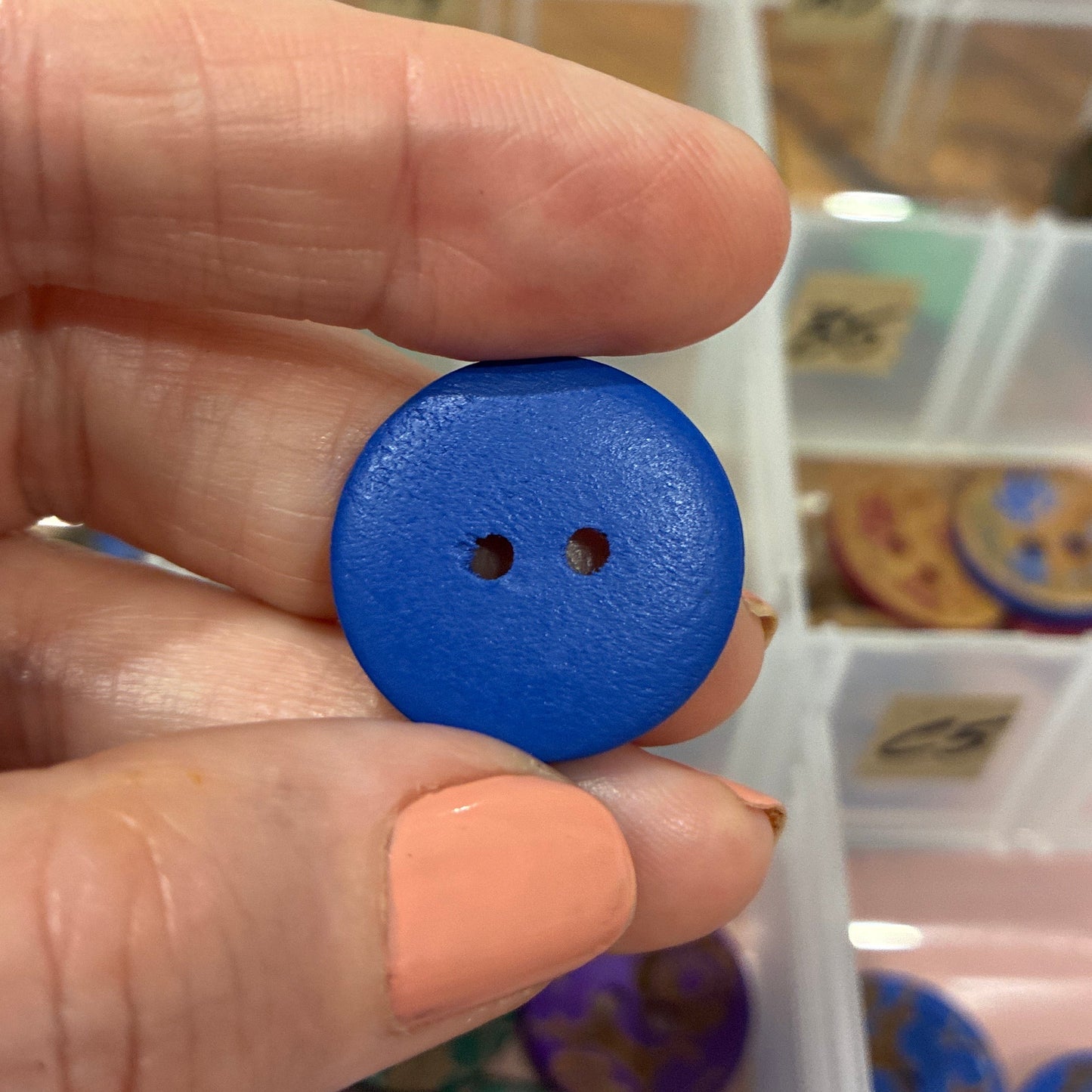 Blue button held between fingers with a container of buttons in the background