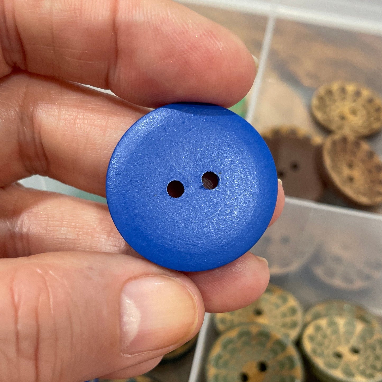 Hand holding a blue button with a collection of buttons in the background