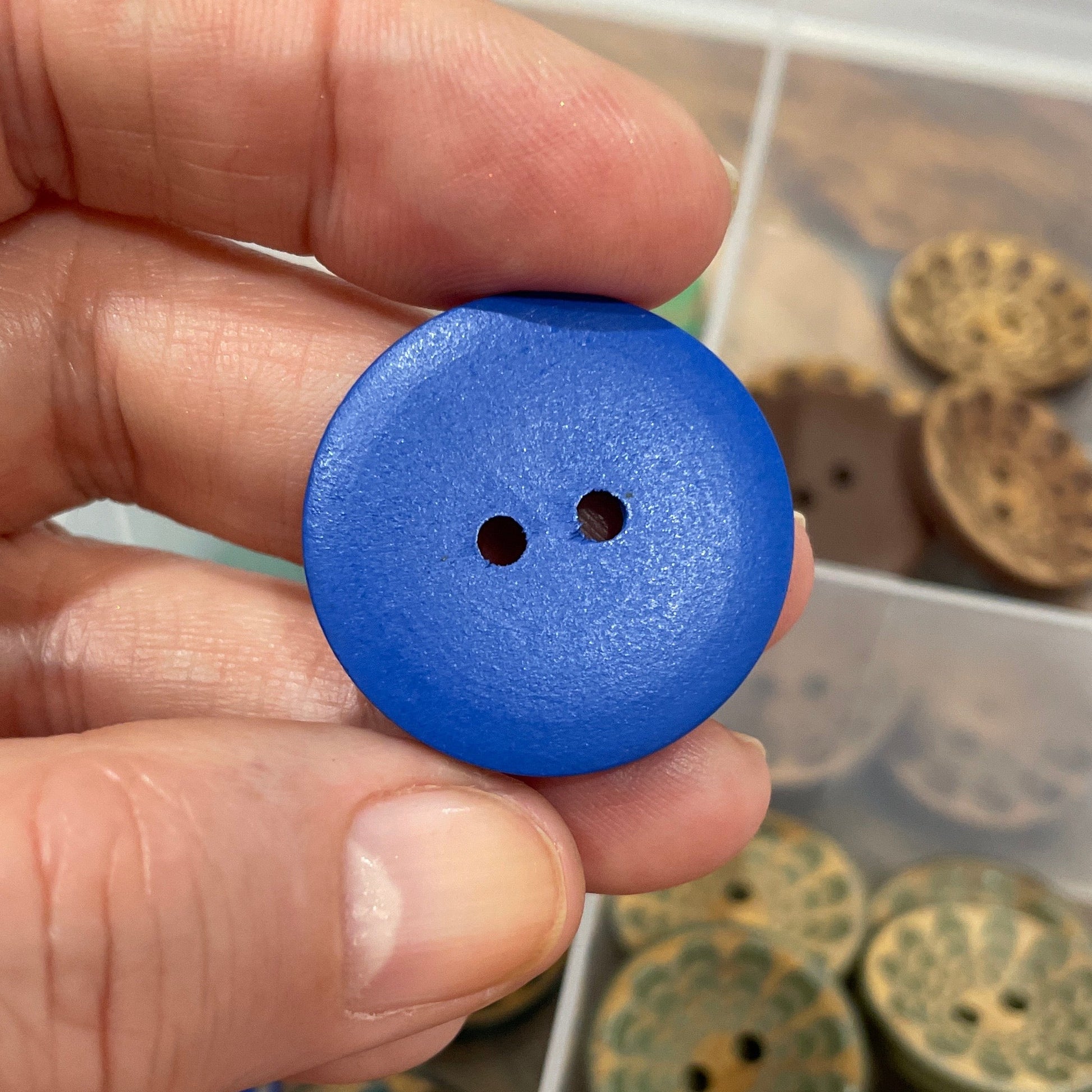 Hand holding a blue button with a collection of buttons in the background