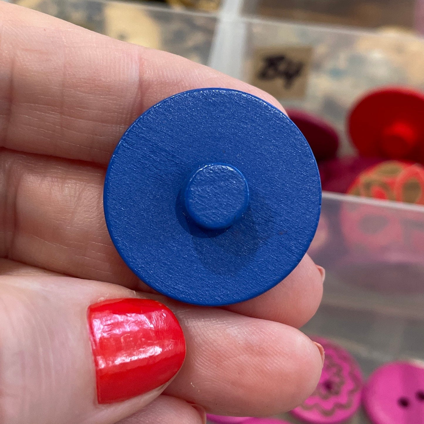 Hand holding a blue button with a container of colorful buttons in the background
