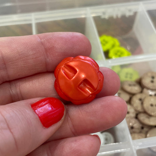 Hand holding two orange buttons with a container of various buttons in the background