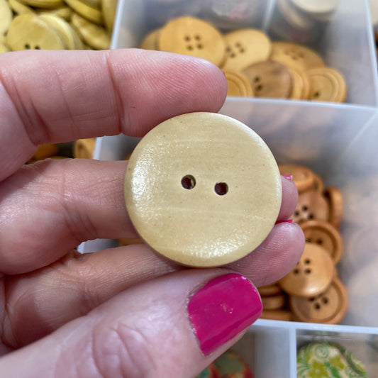 Hand holding a beige button with a clear container of buttons in the background