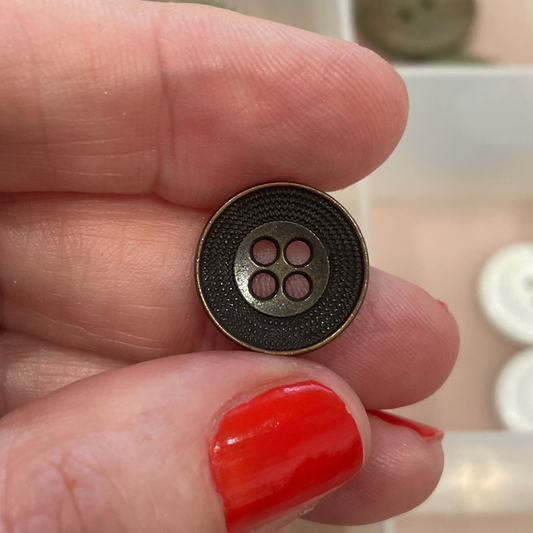 Hand holding a black button with four holes in front of a button organizer.