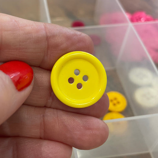 Hand holding a yellow button with a clear container of buttons in the background