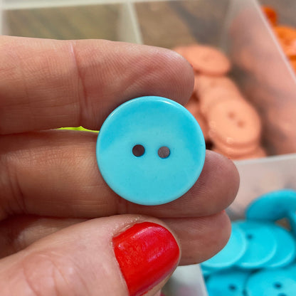 Hand holding a blue button with a blurred background of button containers.