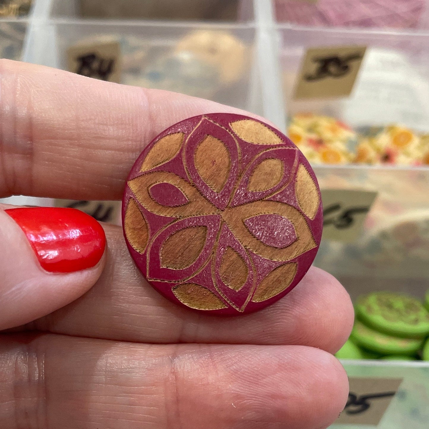 Hand holding a decorative button with a blurred background of button collection