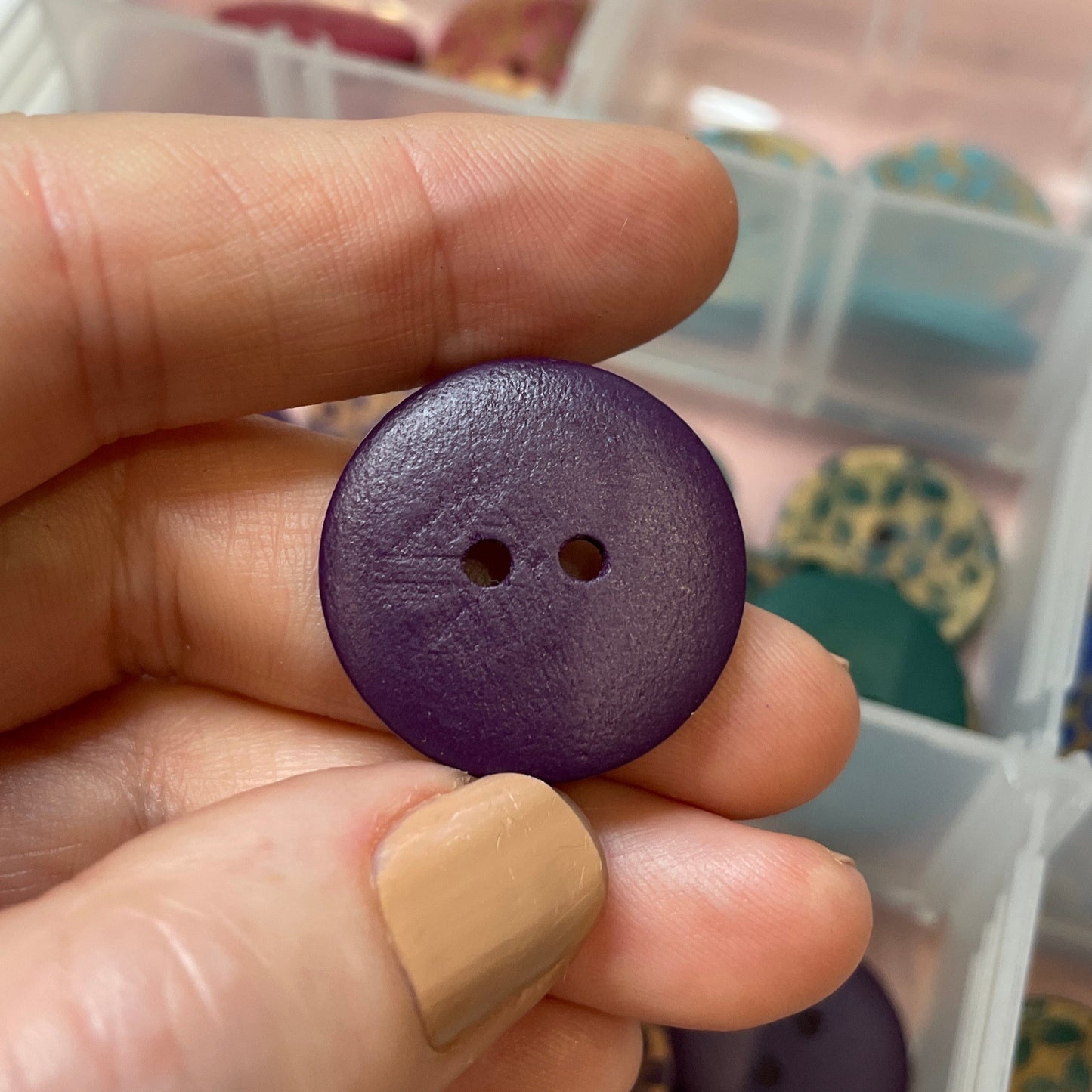 Hand holding a purple button with a container of buttons in the background