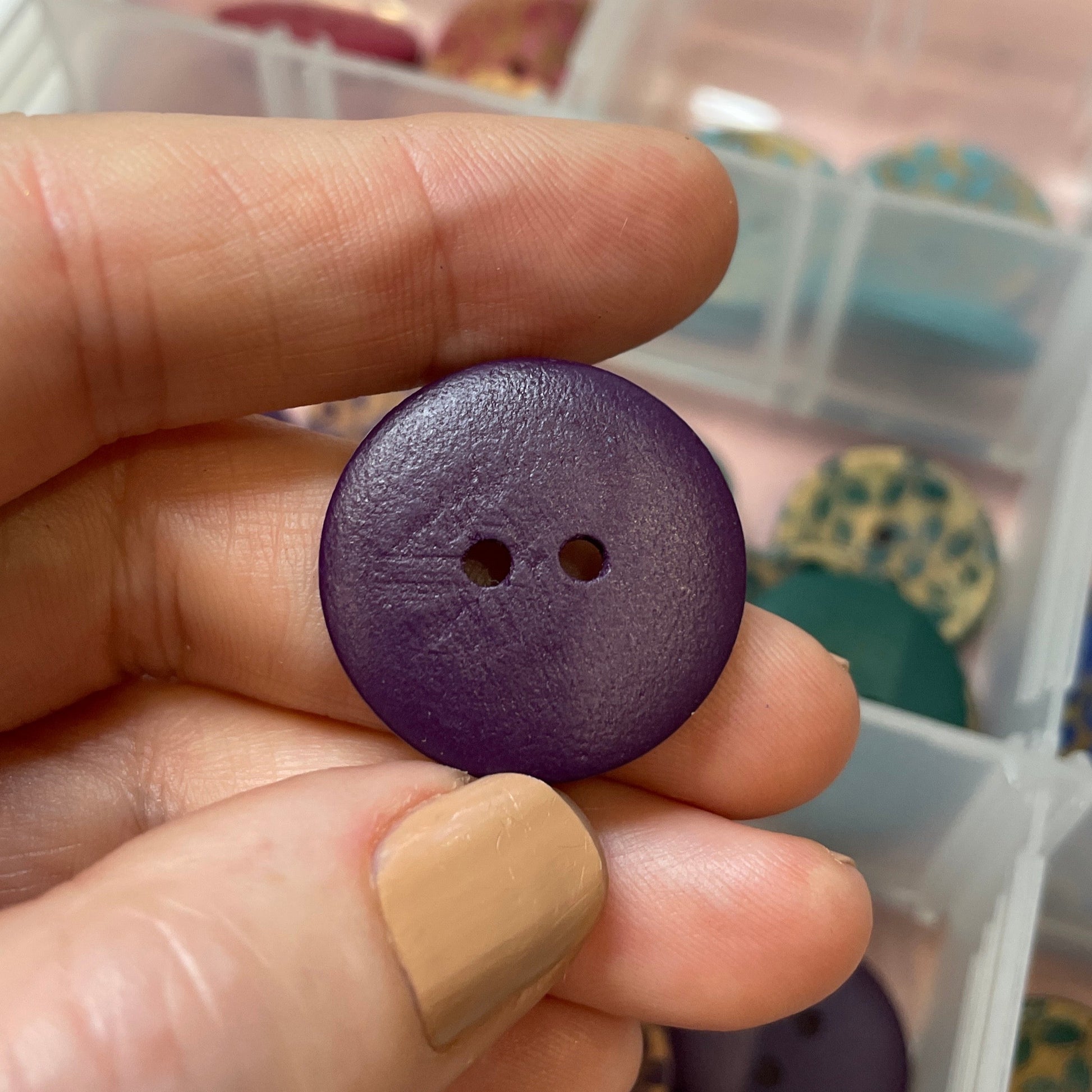 Hand holding a purple button with a container of buttons in the background