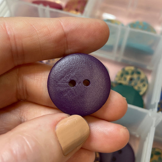 Hand holding a purple button with a container of buttons in the background