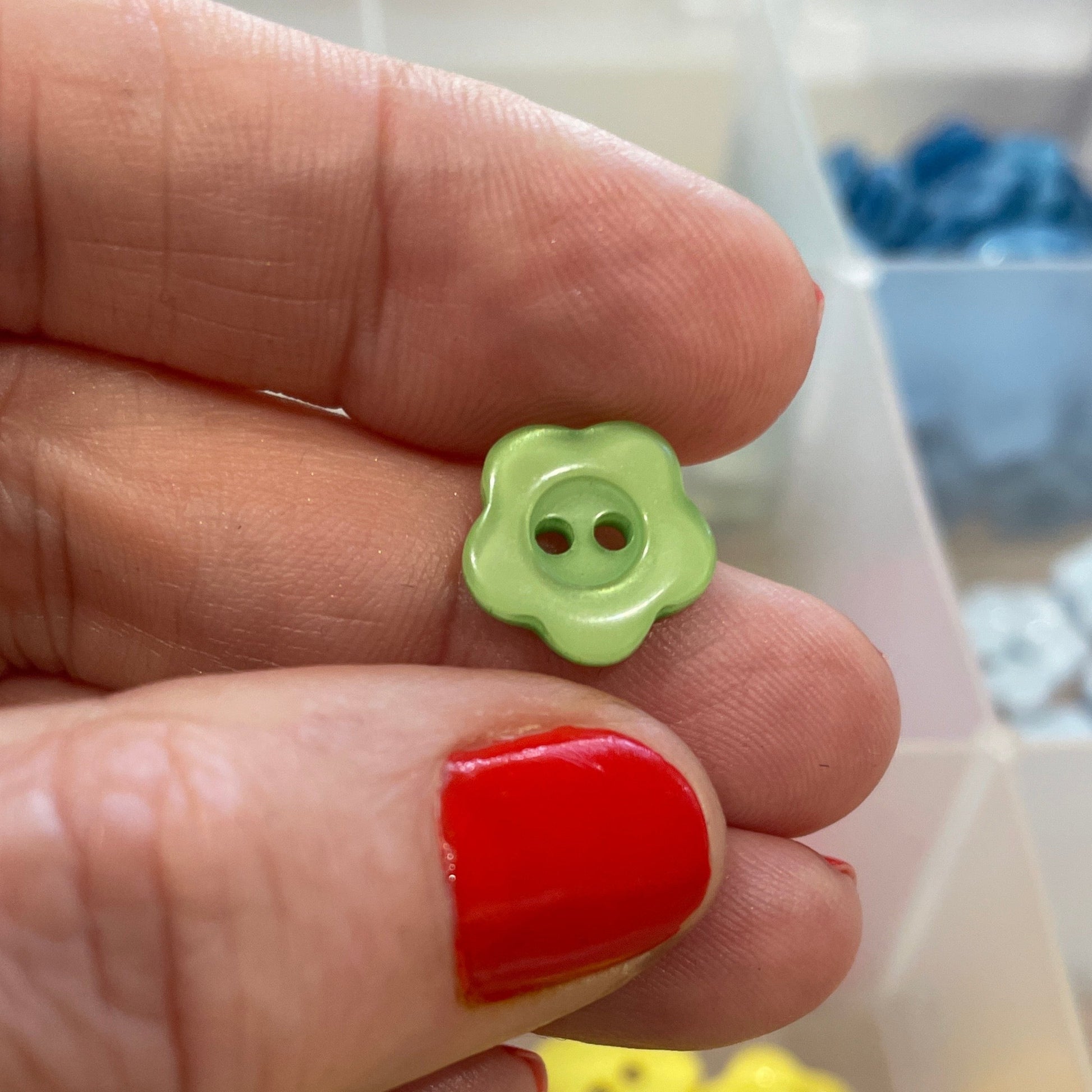 Hand holding a small green button with a box of colorful buttons in the background