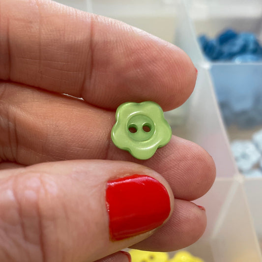 Hand holding a small green button with a box of colorful buttons in the background