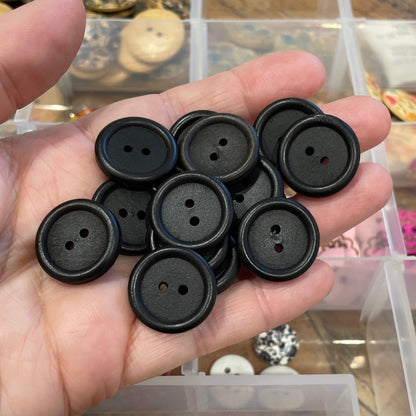 Hand holding black buttons with a container of assorted buttons in the background.