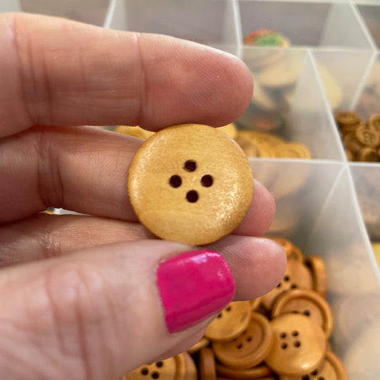 Hand holding a wooden button with a blurred background of button collection