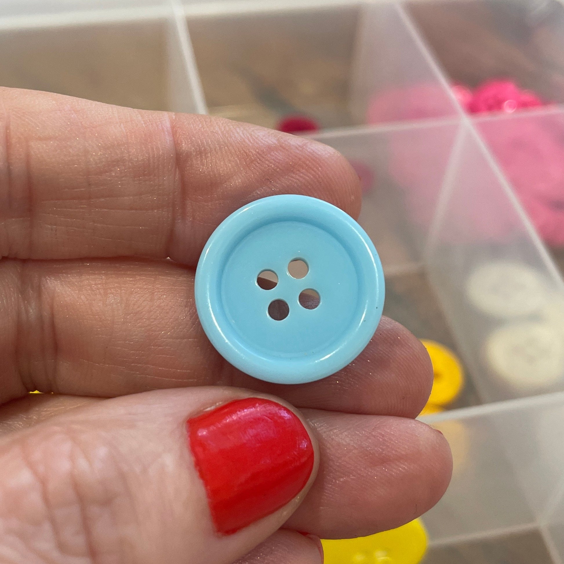 Hand holding a blue button with a clear container of buttons in the background