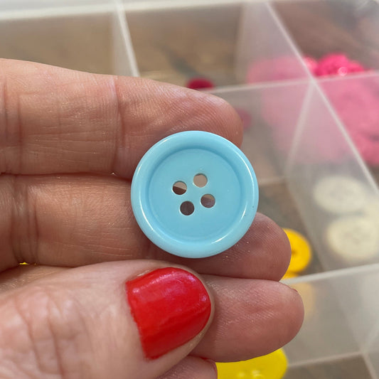 Hand holding a blue button with a clear container of buttons in the background