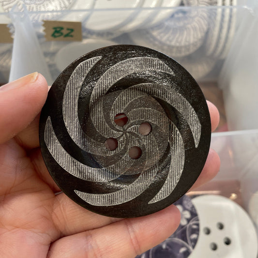 Hand holding a decorative button with intricate design in front of a display of buttons.