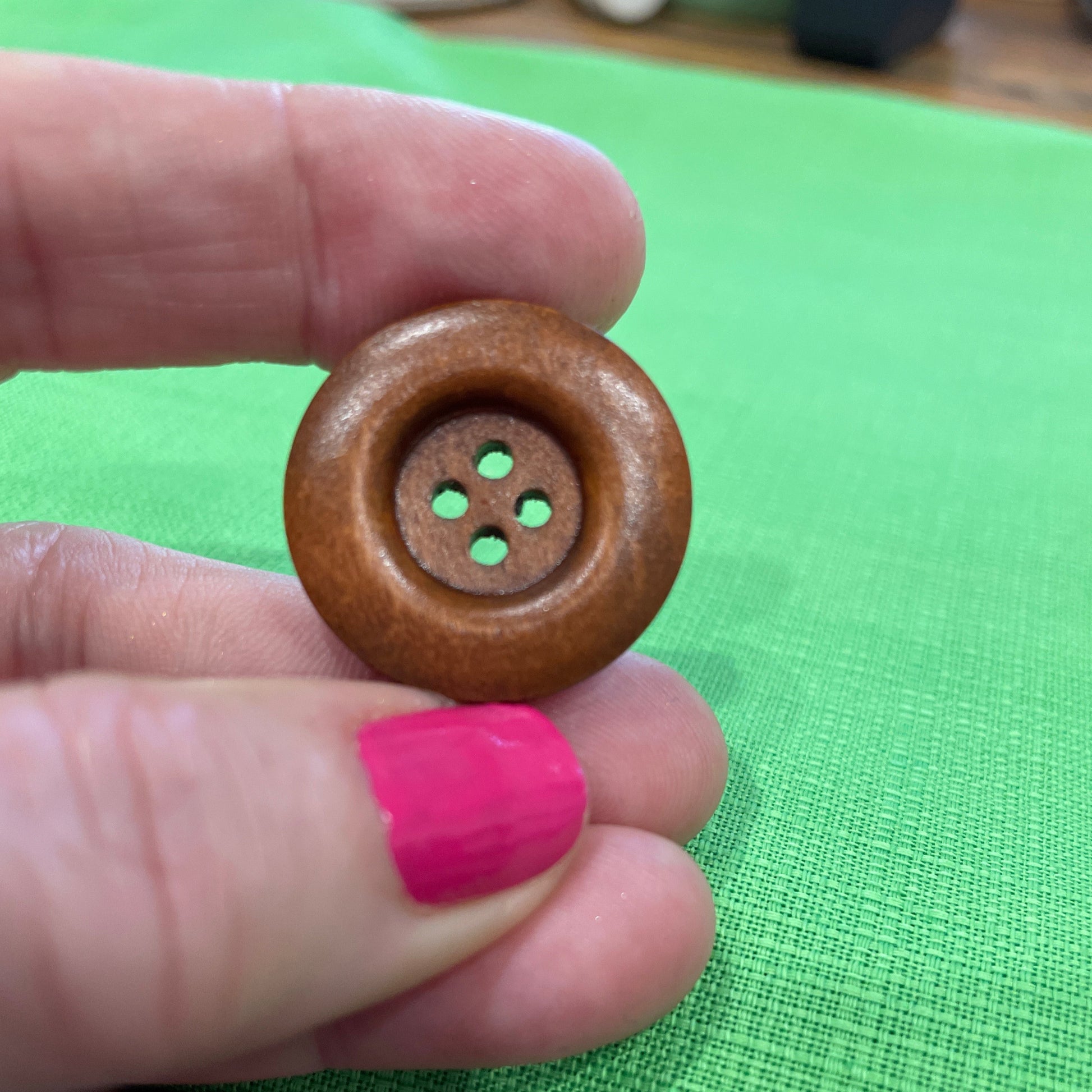 Wooden button held by a hand with pink nail polish against a green fabric background