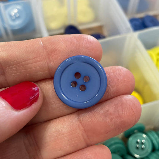 Hand holding a blue button with a container of colorful buttons in the background