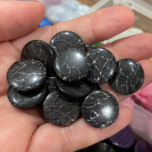 Hand holding black glittery buttons with a container of colorful buttons in the background.