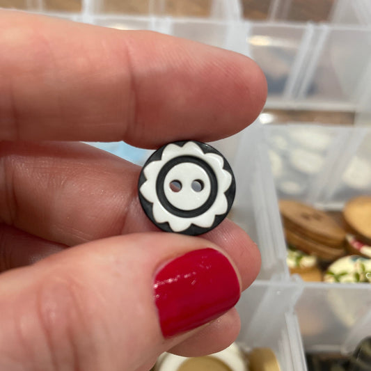 Black and white button held between fingers with a container of buttons in the background