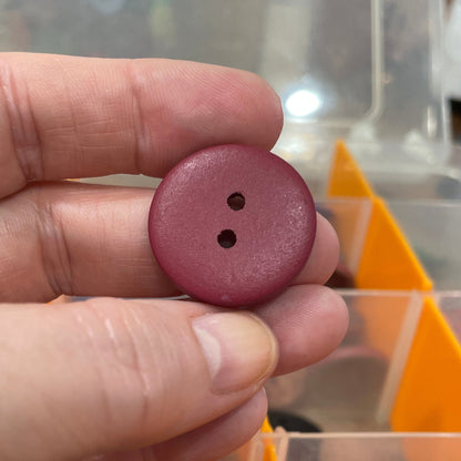 Hand holding a purple button with a container of buttons in the background