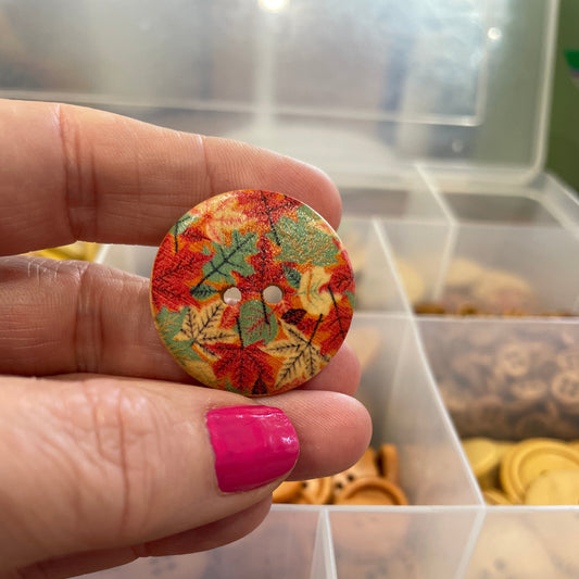 Hand holding a colorful button with floral design in front of a display of similar buttons.