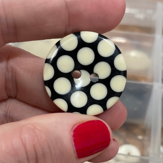 Hand holding a black and white polka dot button with a container of buttons in the background