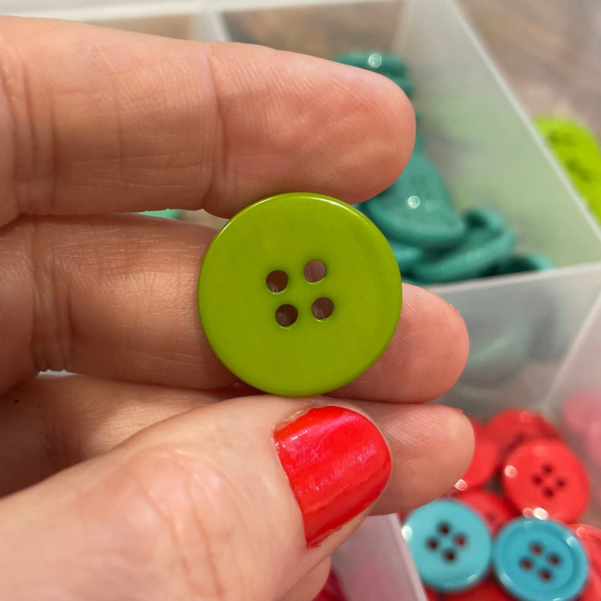 Hand holding a green button with a container of red buttons in the background