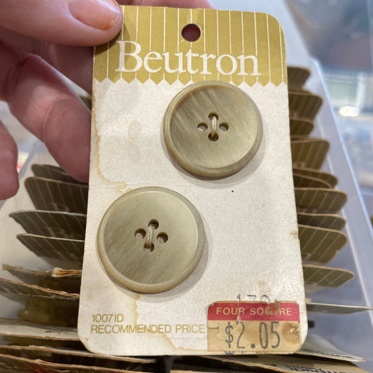 Two buttons on a Beutron card held by a hand with a blurred background.